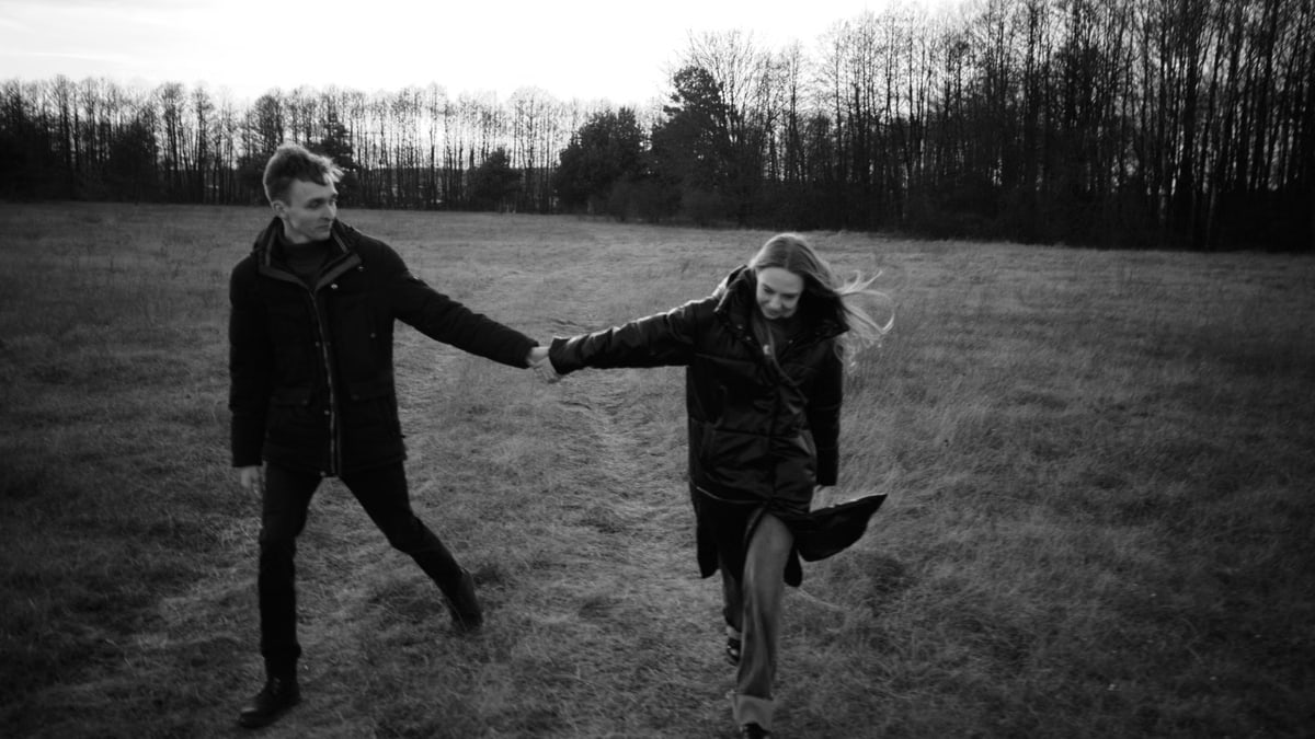 A couple walking hand in hand through a grassy field in black and white, exuding romance.