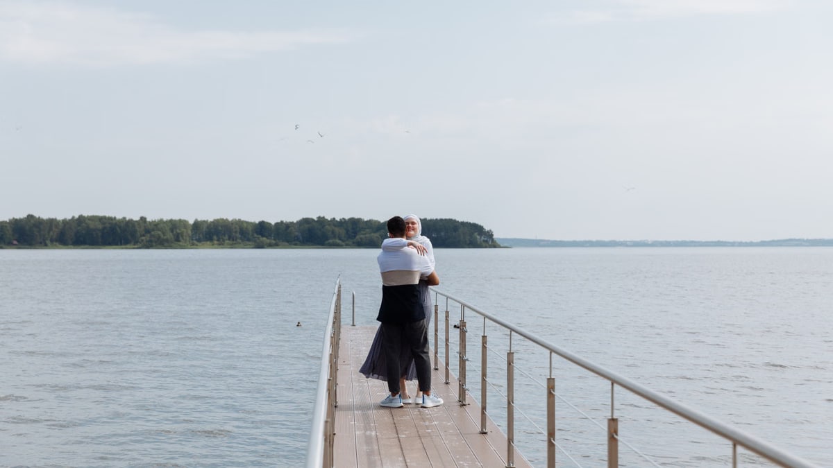 Couple embracing on a wooden dock with serene waterfront views, capturing love and tranquility.